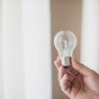 close up mans hand holding transparent light bulb