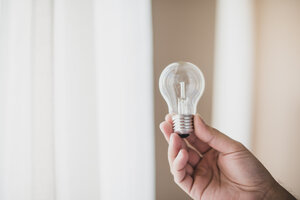 close up mans hand holding transparent light bulb