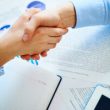 Close-up of female and male handshaking over workplace with business documents