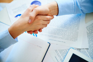 Close-up of female and male handshaking over workplace with business documents