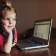 little girl with headphones listening to music, using laptop.