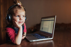 little girl with headphones listening to music, using laptop.