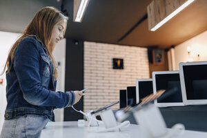 young attractive girl in electronics store stands at desk and tests phone. phones shop. concept of buying gadgets.