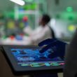 Scientist researcher doctor analyzing genetic mutation test using tablet while her collegue typing biological expertise on computer