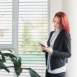 A woman standing near a window with blinds