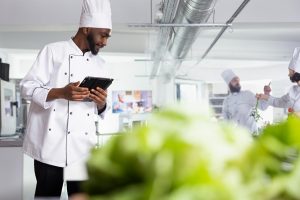 A chef making notes on his technological devices about the food in the kitchen