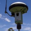 GNSS receiver antenna mounted on a survey tripod against a blue sky, used for centimetre-level positioning