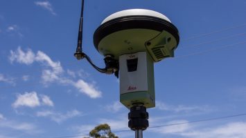 GNSS receiver antenna mounted on a survey tripod against a blue sky, used for centimetre-level positioning