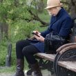 An older woman sitting on a park bench using a smartphone, representing mobile technology that supports ageing in place and keeps families connected