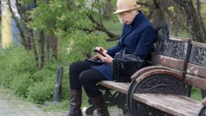 An older woman sitting on a park bench using a smartphone, representing mobile technology that supports ageing in place and keeps families connected